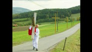 Ein Mann mit Kreuz auf der Schulter geht die Straße entlang  