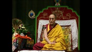 Der Dalai Lama sitzt auf einer Empore  