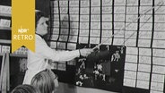 Lehrerin zeigt Kindern an einer mit Klebezetteln bestickten Schultafel Worte (1965)  