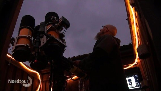 Ein Mann steht neben einem Teleskop, das in den Himmel gerichtet ist.  