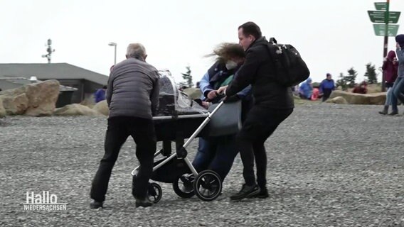 Auf dem Brocken sichert eine Familie einen Kinderwagen gegen die Sturmböen.  