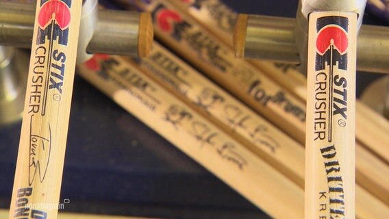 Nahaufnahme von handgefertigten Drumsticks, die Unterschriften bekannter Musiker drauf haben.  