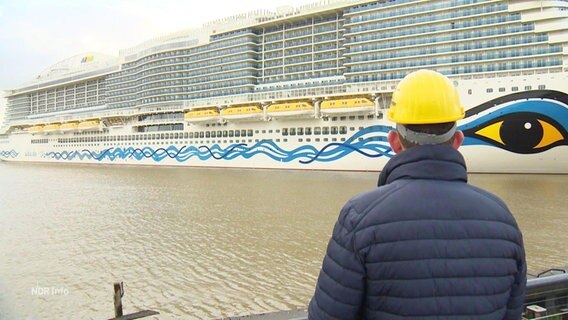 Ein Werftmitarbeiter schaut auf ein Aida-Kreuzfahrtschiff. 