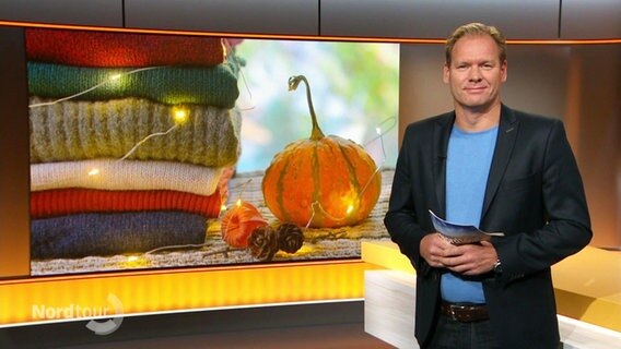 Moderator Thilo Tautz, im Hintergrund ein Bild mit Wolldecken und einem Kürbis.  