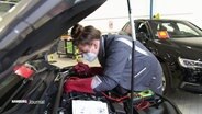 Eine Auszubildende zur Kfz-Mechatroniker unter der Motorhaube eines Autos  