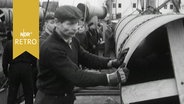 Mehrere Arbeiter stehen neben einem großen Rohr (Pipeline) bei der Verladung im Hafen 1960  