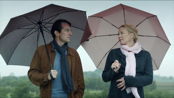Ein Mann (Hans-Werner Meyer) und eine schwangere Frau (Katja Riemann) unter Regenschirmen, sie schauen sich an. Sie hat ihre Hand auf ihrem Bauch.  