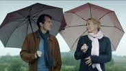 Ein Mann (Hans-Werner Meyer) und eine schwangere Frau (Katja Riemann) unter Regenschirmen, sie schauen sich an. Sie hat ihre Hand auf ihrem Bauch.  