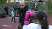 Kareem Ahmed von der Silbersack Hood Gym beim Box-Training mit einem Mädchen, draußen auf einem Sportplatz.  