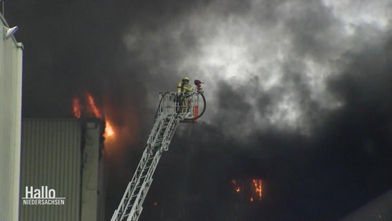 Feuerwehrleute stehen auf einer Leiter vor einer großen Rauchwolke.  