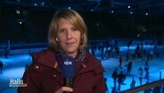 Reporterin Birte Olig berichtet von der Eisdisco in Wolfsburg, im Hintergrund sieht man Schlittschuhläufer in einer Eishalle.  
