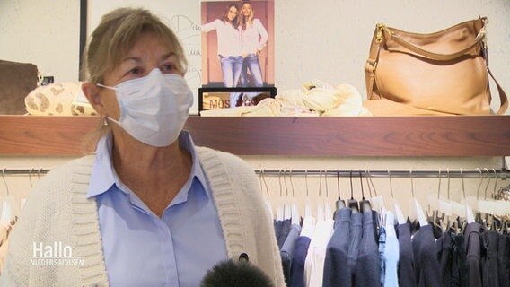 Eine Frau mit OP-Maske vor einem Kleiderregal in einer Boutique  