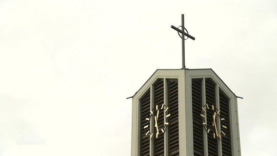 Ein Kreuz steht auf der Spitze eines Kirchenturms.  
