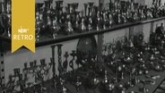 Divers kleine Vasen, Kerzenständer und andere Messingwaren als fernöstliche Geschenkartikel auf drei Regalbrettern (1964)  