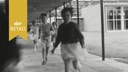 Kinder laufen einen Laubengang in einer Schule entlang (1964)  