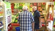 Zwei ältere Herren vor dem Gemüseregal eines Dorfladens  