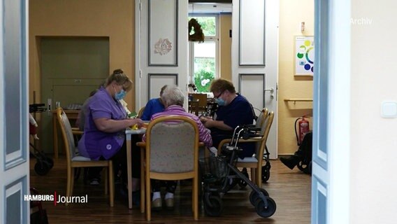 Blick in eine Pflegeeinrichtung mit mehreren Personen an einem Tisch.  
