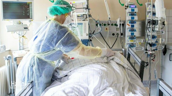 Eine Intensivpflegerin steht am Bett eines Patienten.  