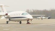 Auf dem Rollfeld eines Flughafens steht ein kleinerer Jet.  