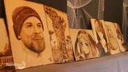 Holzplatten mit verschiedenen Brandzeichnungen, unter anderem Porträts im Anime-Stil und das Bild einer Giraffe.  