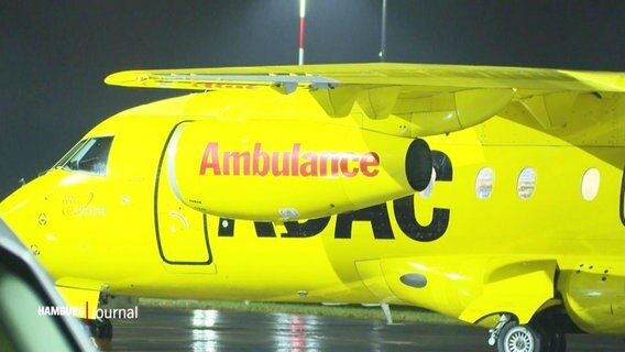 Ein gelbes Flugzeug mit der Aufschrift "Ambulance" steht im Dunkeln auf einem Rollfeld.  