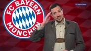 Ein Mann mit Lederhose vor dem Vereinsemblem des FC Bayern München  