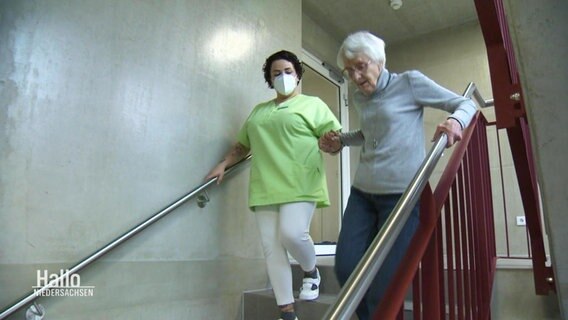 Pflegerin begleitet ältere Dame die Treppe herunter.  