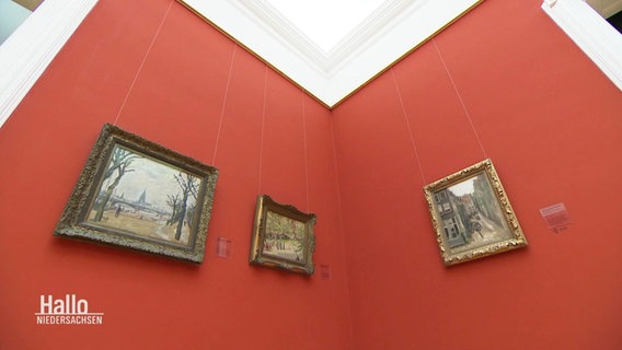 Blick auf rot gestrichene Wände in einer Ausstellung. Daran hängen drei Gemälde im kleinen Format.  