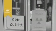 Schilder an der Glastür zu einem Labor: "Kein Zutritt" - "Vorsicht Radioaktiv" (1963)  
