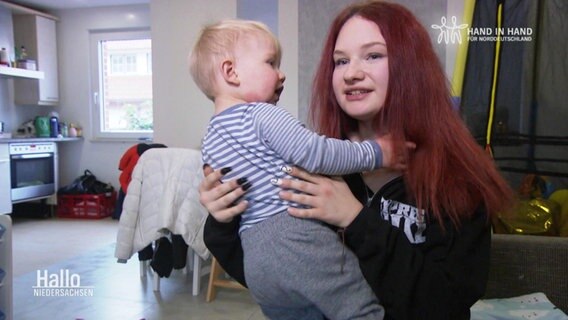 Eine junge Frau mit einem blonden Kleinkind auf dem Arm. © Screenshot 