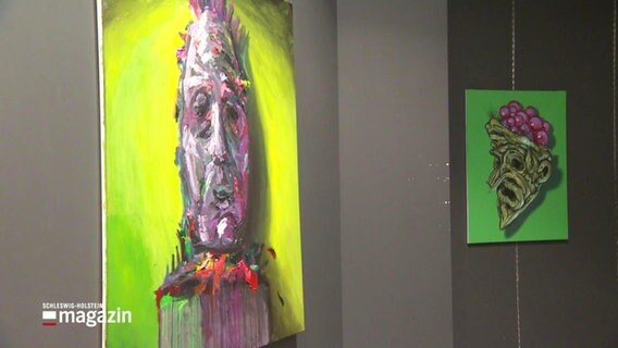 Blick auf zwei Gemälde in grellen Farben. Beide bilden jeweils einen grotesken, maskenartigen Kopf ab. © Screenshot 