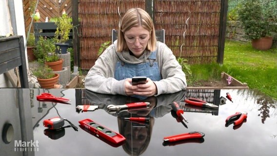 Frau am Smartphone mit Werkzeug auf dem Tisch. © Screenshot 