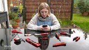 Frau am Smartphone mit Werkzeug auf dem Tisch. © Screenshot 