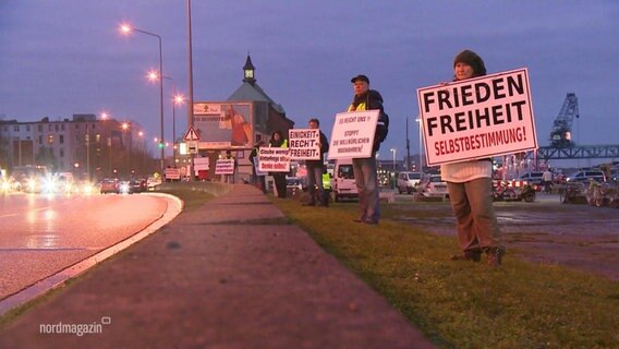 In Rostock stehen Demonstranten mit großen Schildern gegen Corona-Maßnahmen an einer Straße. © Screenshot 
