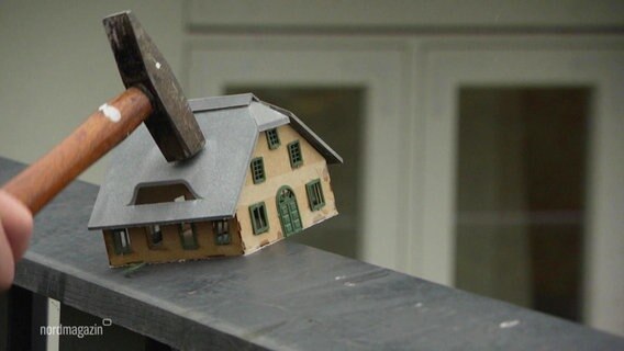 Ein Hammer schlägt auf eine Modellhaus. © Screenshot 