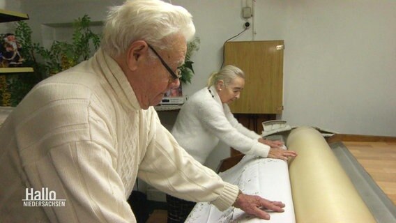 Ein älteres Ehepaar schiebt eine Decke in eine Heißmangel. © Screenshot 