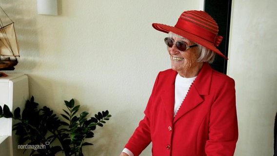 Eine der Teilnehmerinnen von "Jahrhundertleben" in einem roten Outfit mit Strohhut. © Screenshot 
