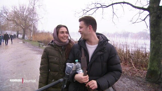 Ein Paar wird bei einem Spaziergang an der Außenalster interviewt, sie lächeln sich zu. © Screenshot 