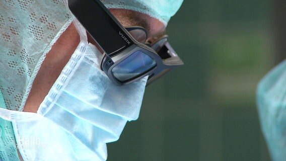 Ein Arzt in OP-Kleidung trägt über seiner Brille eine schwarze Cyberbrille. © Screenshot 
