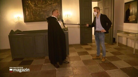 Reporter Philipp Jeß interviewt einen Mann, der die Robe eines Scharfrichters trägt. © Screenshot 