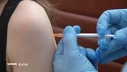 Eine Impfspritze wird in einen Arm injiziert. © Screenshot 