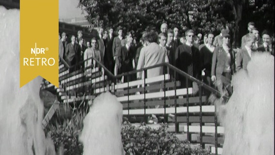 Zahlreiche Jugendliche kommen eine Treppe herunter, davor drei Fontänen auf dem IGA-Gelände in Planten un Blomen in Hamburg 1963 © Screenshot 