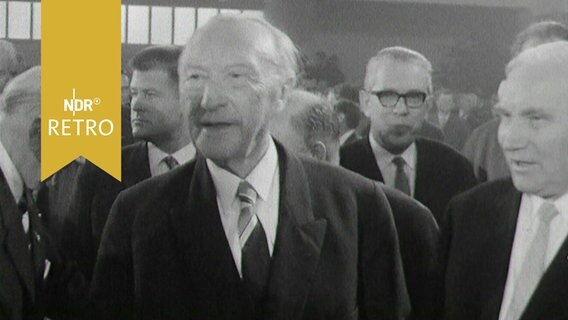 Bundeskanzler Konrad Adenauer zwischen anderen Männern in einer Veranstaltungshalle (Deutscher Bauerntag 1963) © Screenshot 