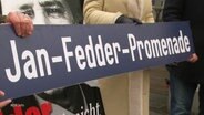 Drei Personen halten ein Schild mit der Aufschrift: Jan-Fedder-Promenade. © Screenshot 