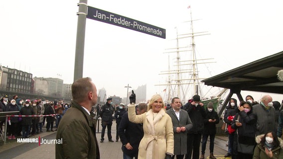 Jan Fedders Witwe, Marion Fedder, zeigt auf das neu angebrachte Straßenschild. © Screenshot 