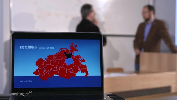 Eine Grafik zeigt die Stimmenverteilung bei der Landtagswahl. Im Hintergrund stehen zwei Personen in einem Hörsaal. © Screenshot 