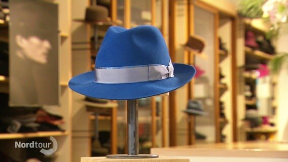Ein blauer Hut wird in einem Hutladen auf einer Stange präsentiert. © Screenshot 