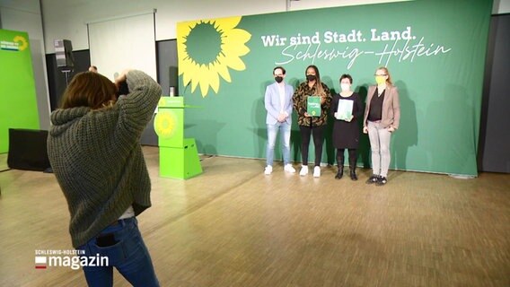 Grünen-Politiker vor einem Plakt mit der Aufschrift Wir sind Stadt.Land.Schleswig-Holstein © Screenshot 
