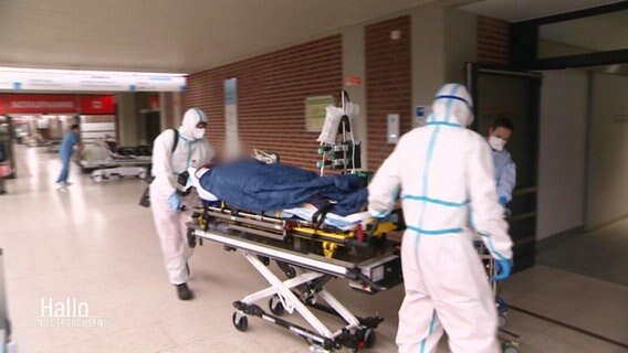 Menschen in Schutzanzügen schieben ein Krankenbett mit einer Patientin © Screenshot 