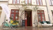 Der Lebensmittelladen MV Liebe von Vanessa Kerstings in Wismar; von außen mit Fahrrad und Bank davor. © Screenshot 